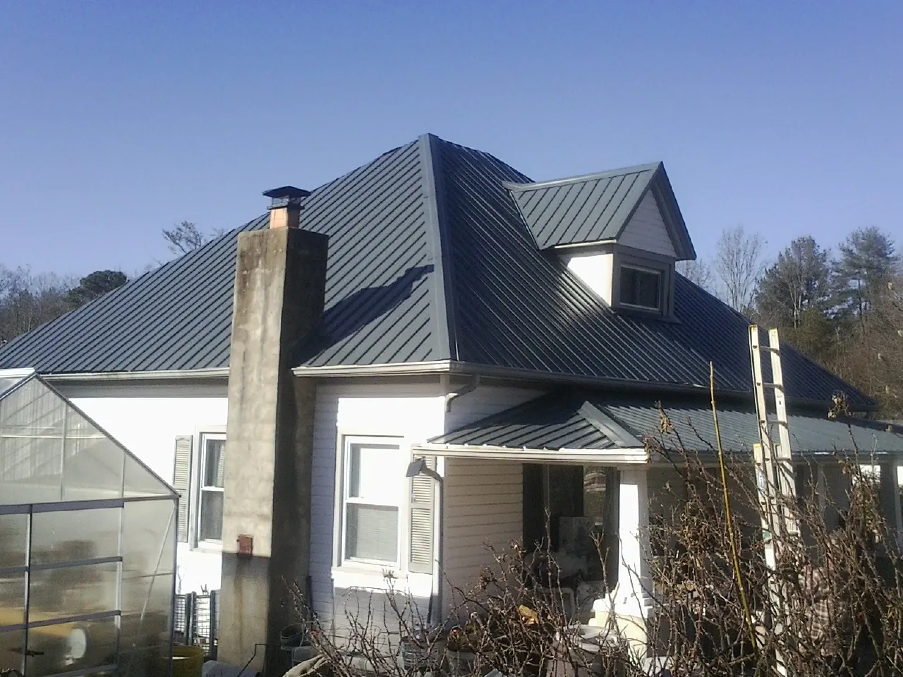 Dark blue standing seam metal roof on a white farmhouse with dormer — Slate & Tile Roof Repair by Roofing Brothers in South Solon