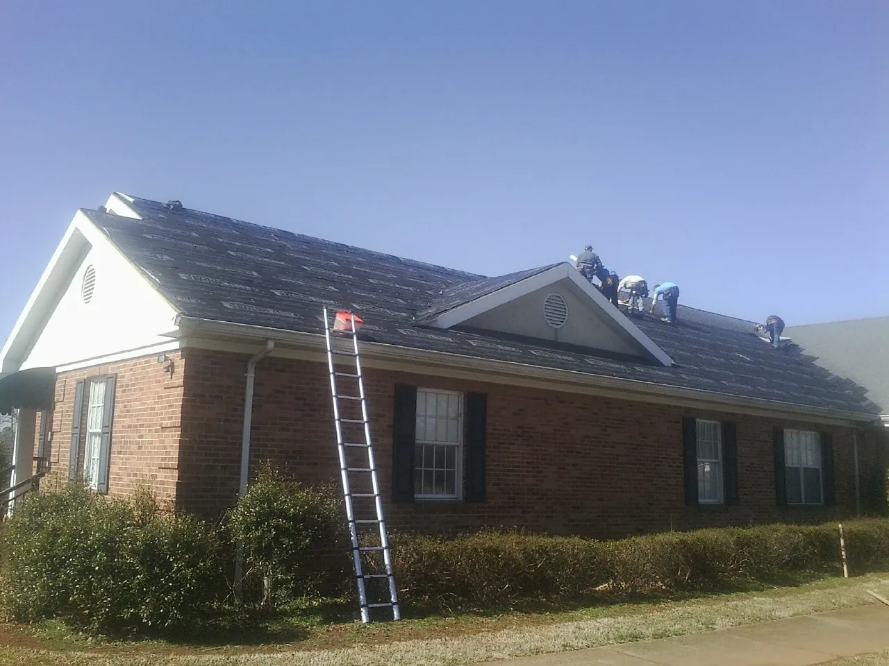 Crew tearing shingles off a brick ranch roof with a ladder set — Emergency Roof Repair work by our crew in South Solon