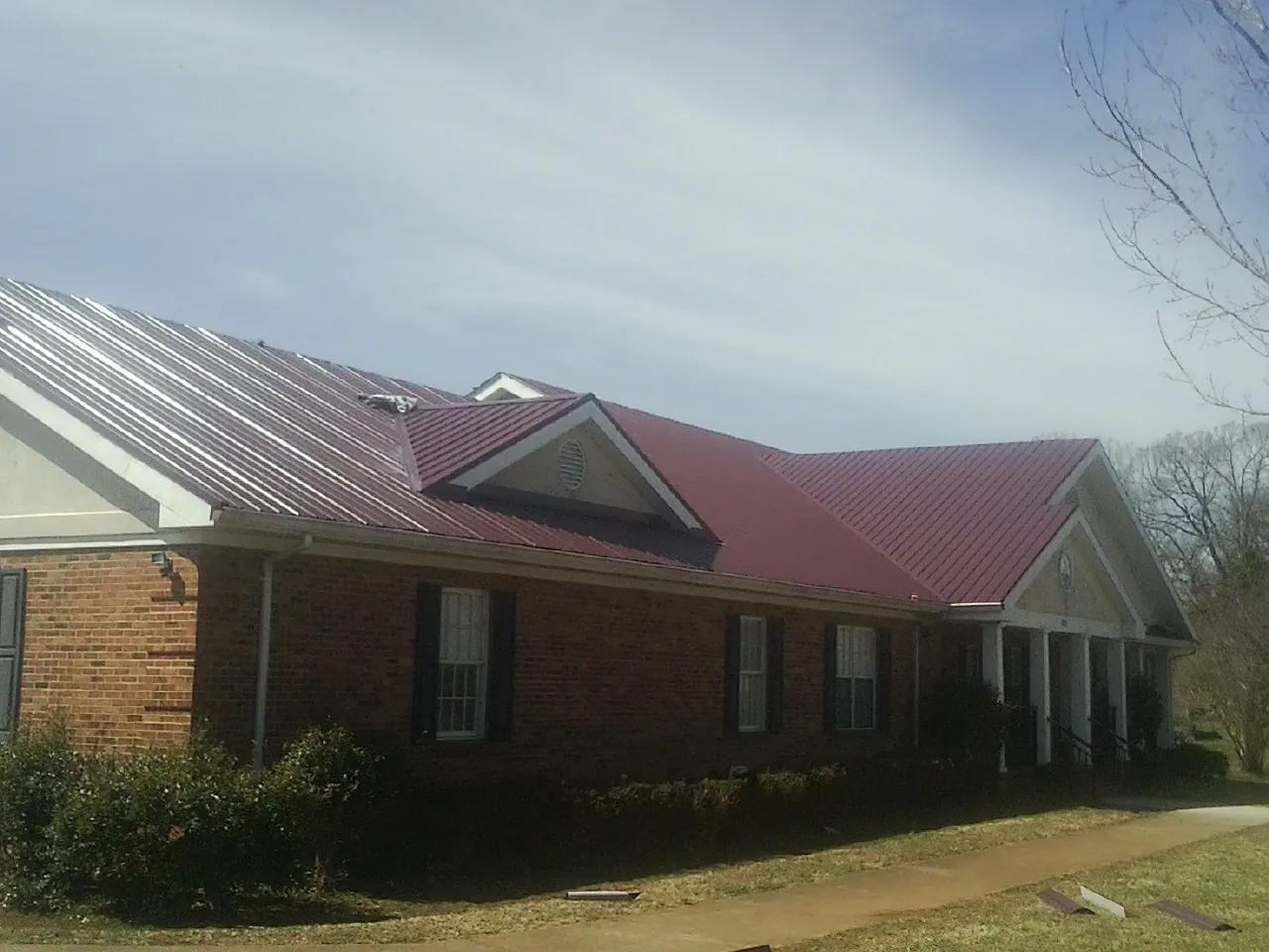 Red metal roof with gabled entries on a long brick building, from a Hail Damage Roof Repair job in South Solon