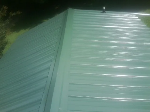 New green metal panels meeting at the ridge of a roof — Flat Roof Repair work by our crew in South Solon