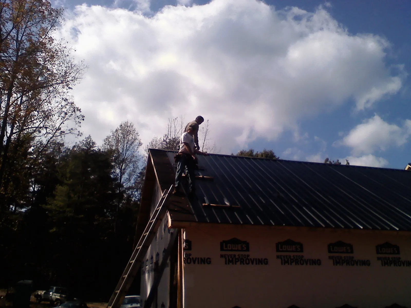 Roofer fastening dark metal panels high against a cloudy sky, from a Roof Inspection job in South Solon