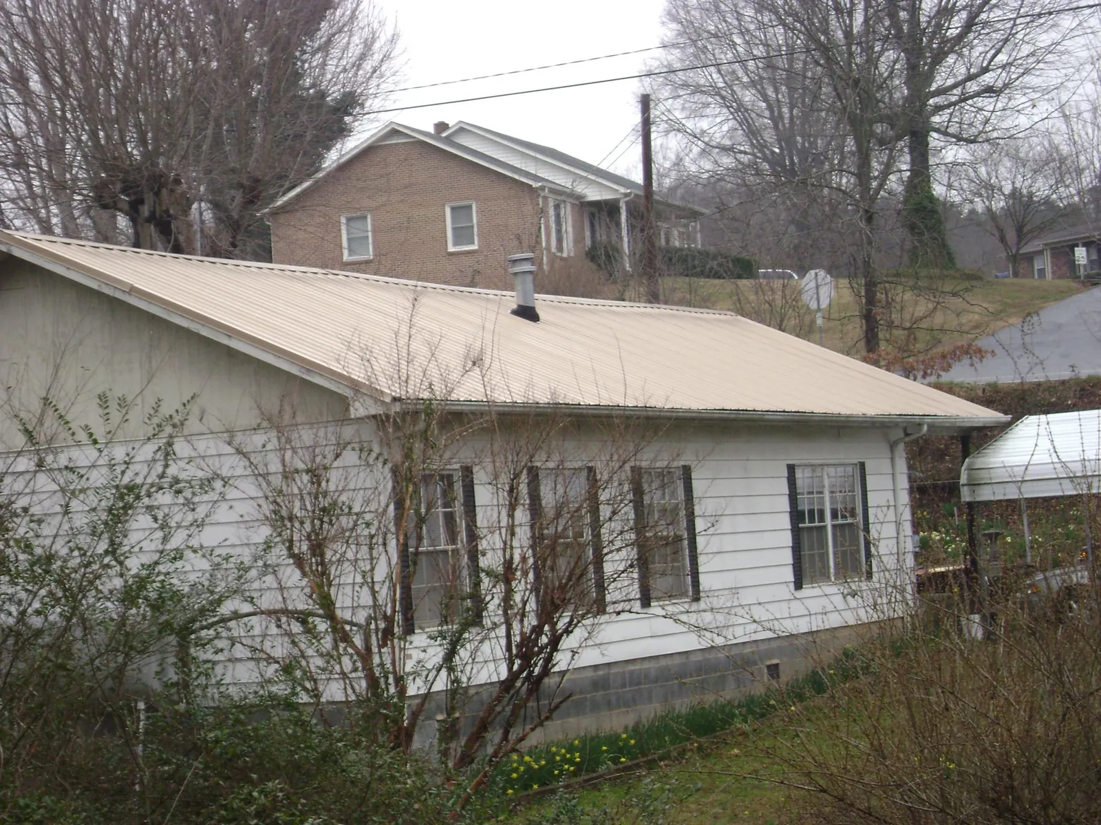 Tan metal roof on a white sided house set into a hillside — Commercial Roofing by Roofing Brothers in South Solon