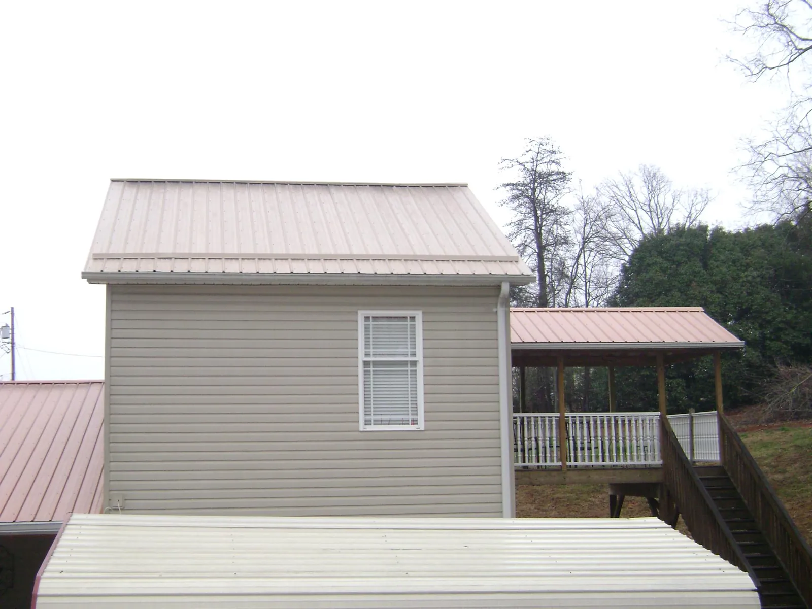 Tan metal roofs on a two story addition and attached porch, from a Roof Replacement job in South Solon